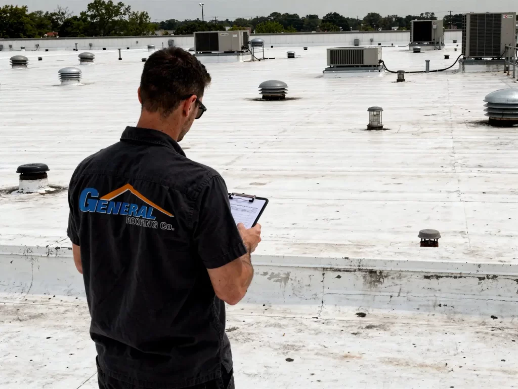 Commercial roofing contractor inspecting a flat TPO roof with rooftop equipment while reviewing inspection notes