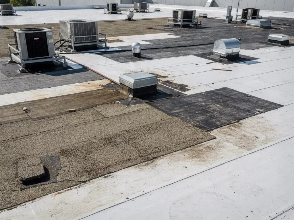 Commercial flat roof showing patchwork repairs with TPO, EPDM, and built-up roofing materials around HVAC units