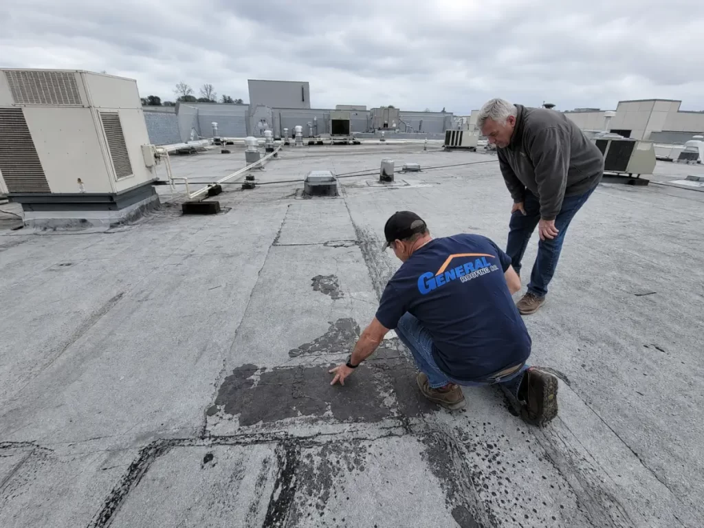 General Roofing technician and property manager inspecting patched areas on a commercial flat roof.