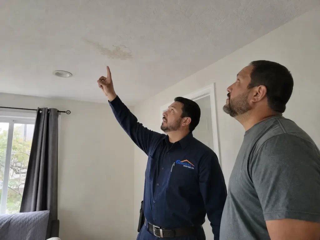 General Roofing roofer pointing out a ceiling water stain that may indicate a roof leak.