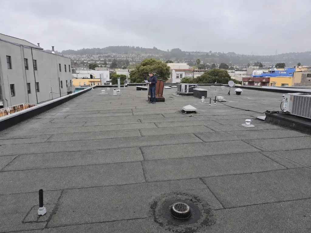 Weathered modified bitumen commercial roof in the Bay Area with rooftop equipment, drainage details and restricted urban access.