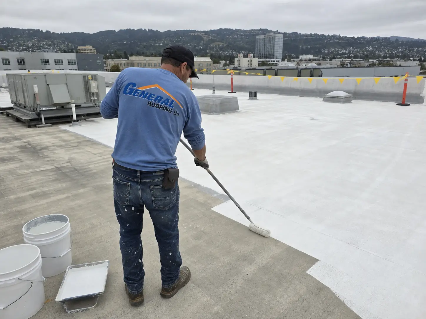General Roofing roofer applying white elastomeric roof coating to a commercial flat roof in the San Francisco Bay Area.
