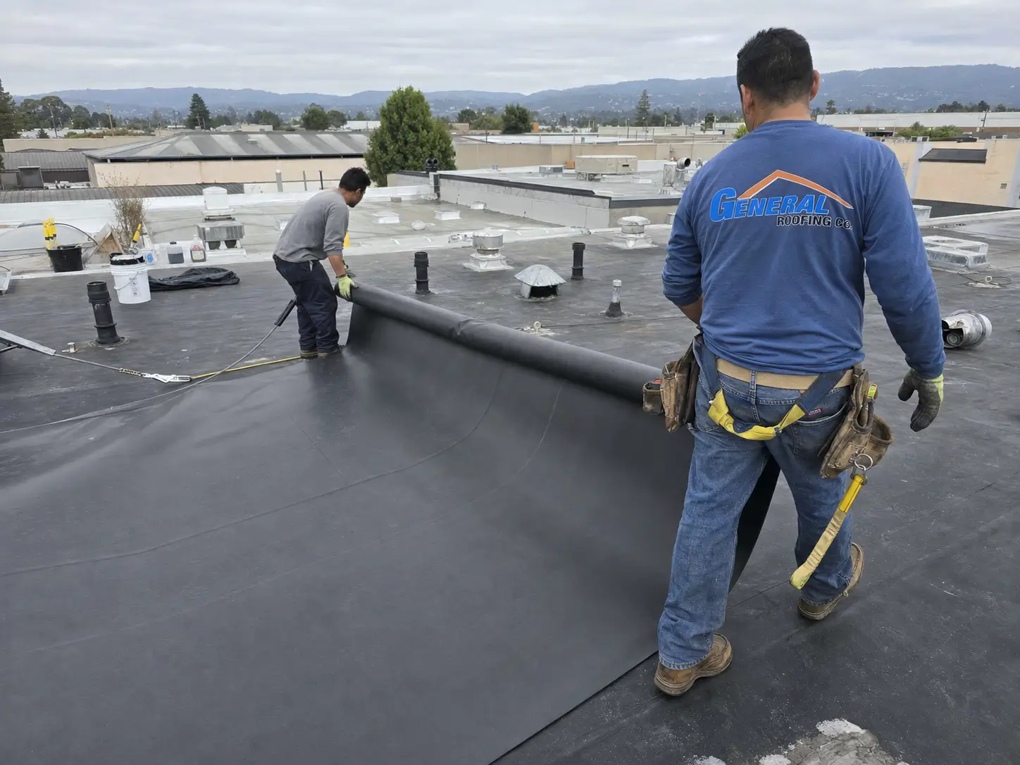 General Roofing roofers install black EPDM membrane on a Bay Area commercial flat roof for a 2026 roofing cost guide.