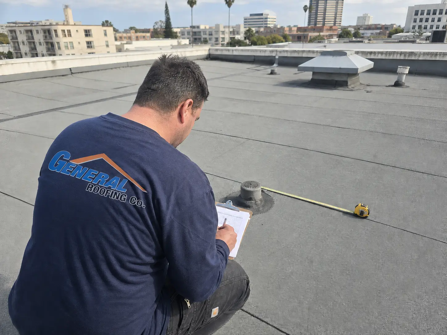 General Roofing contractor measures a modified bitumen roof while preparing a 2026 price-per-square-foot estimate.