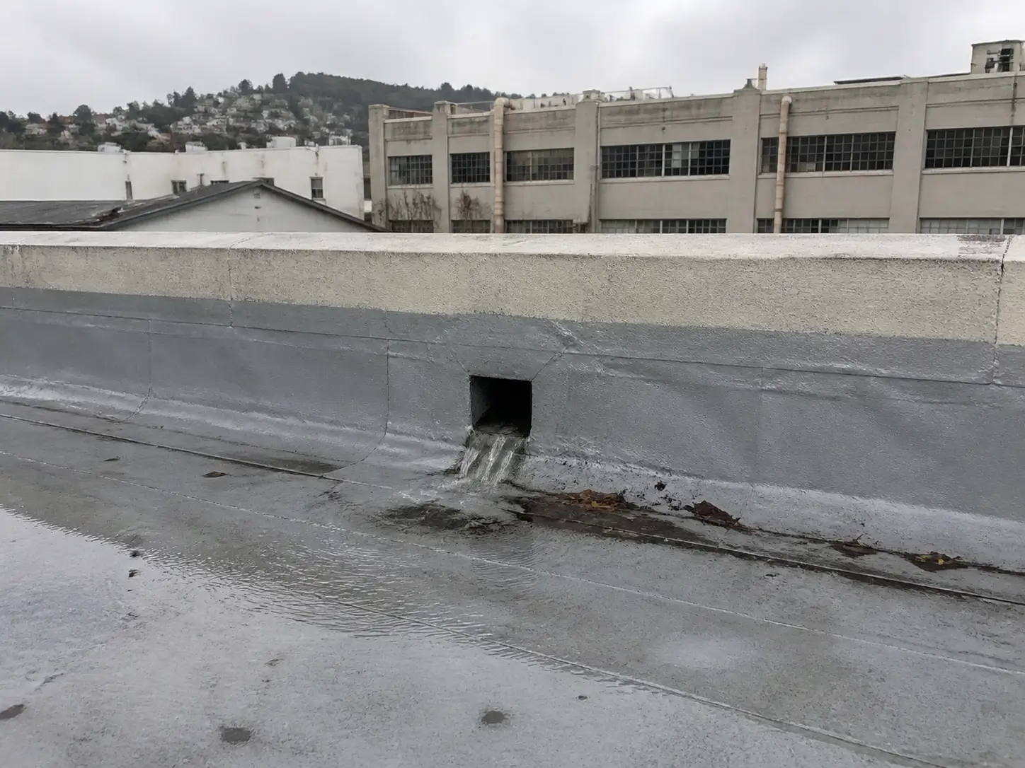 Rainwater flows through a metal roof scupper in a parapet wall on an older Oakland commercial building.