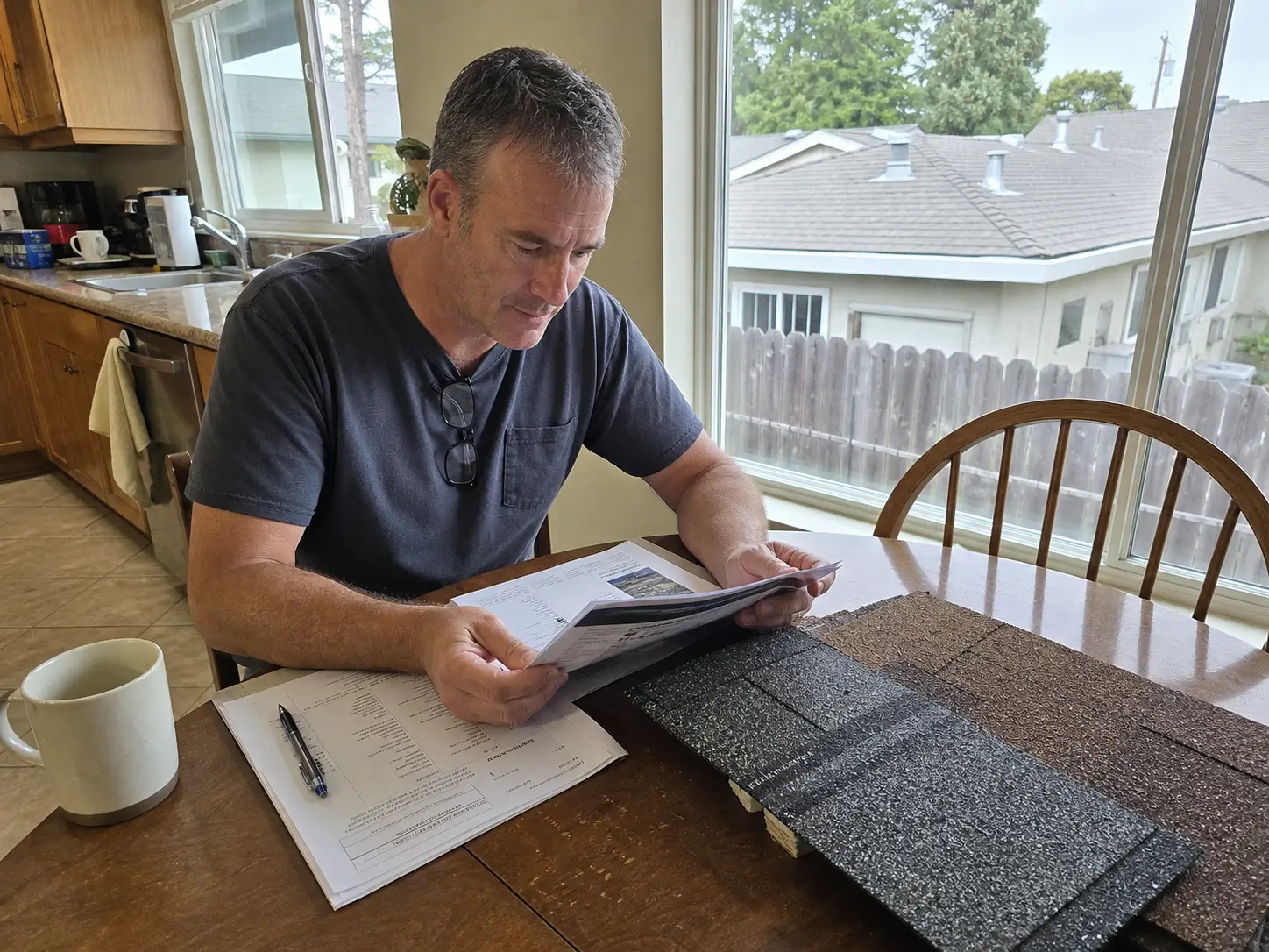 Bay Area homeowner reviews roof warranty documents and shingle samples at a kitchen table.