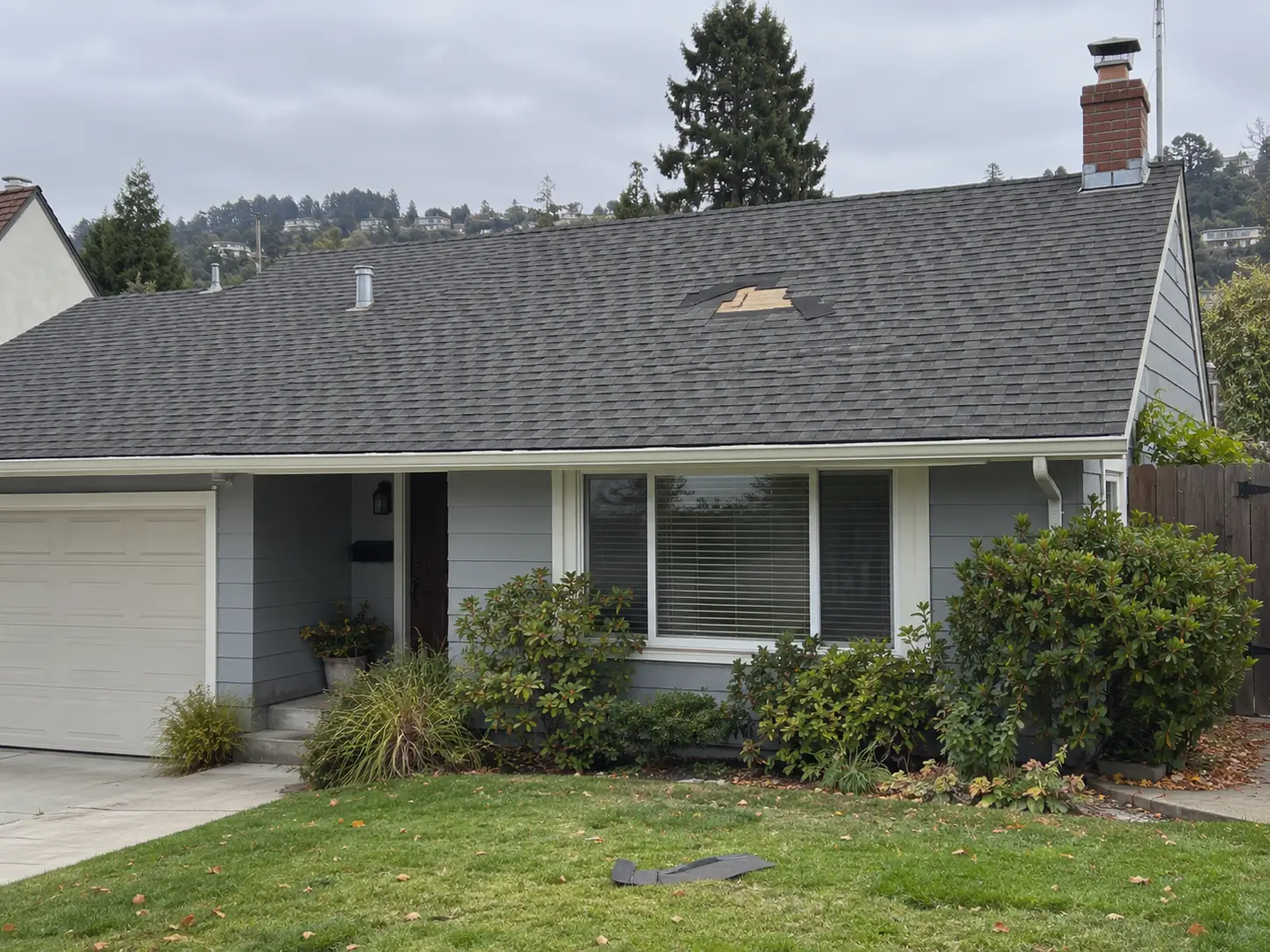 Oakland home with a patch of missing asphalt shingles on the roof and blown-off shingles in the yard.